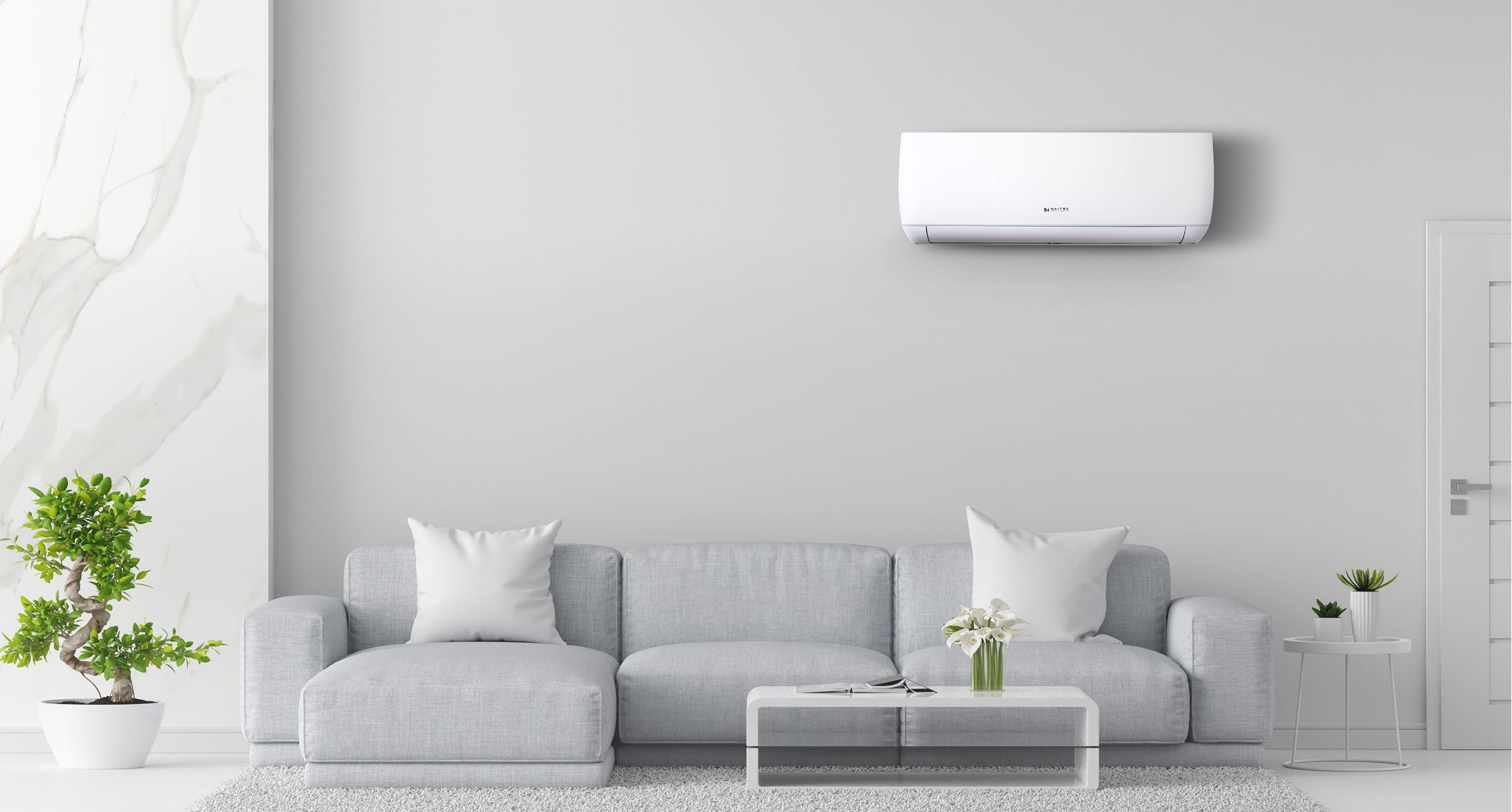 Ein modernes Wohnzimmer mit einem hellgrauen Sofa, einem gläsernen Couchtisch, Topfpflanzen und einer an der Wand befestigten Klimaanlage